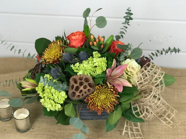 Unconventional yet a warm reminder of what Thanksgiving could be. A simple, rustic design for a centerpiece for the Thanksgiving table. Warm tones and lots of texture fill up this tin container. Kale, hydrangea, roses, thistle, lilies, leucadendron, eucalyptus, hypericum and mums. Done by Gig Morris Florist in Belmar, New Jersey.