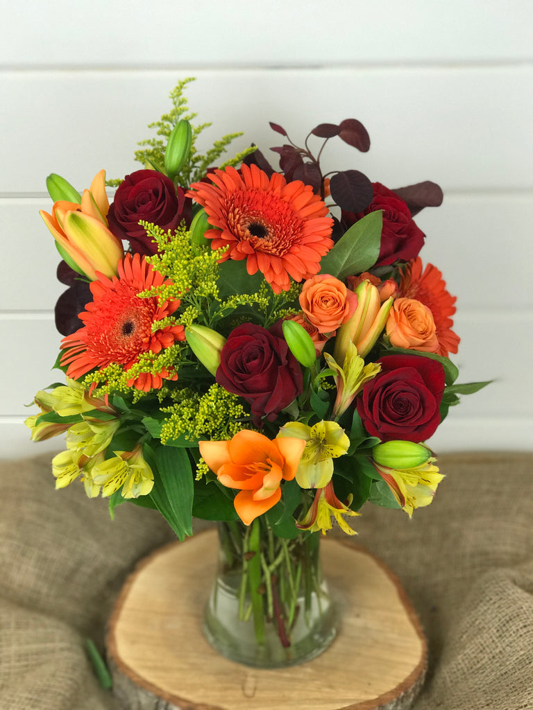 Fall flowers in vase arrangement. Roses, Gerber daisies, lilies in oranges, reds, and yellows